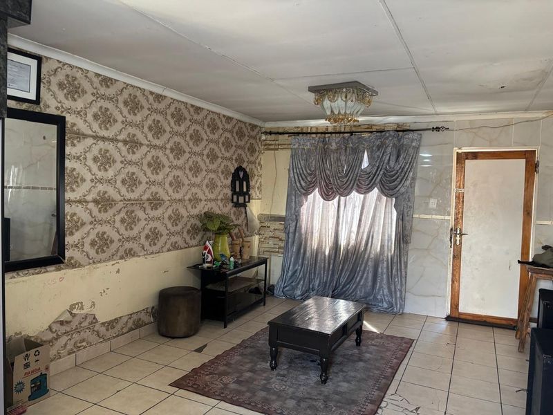 A living room featuring tiled flooring and decorative wallpaper, currently showing signs of wear and requiring cosmetic updates to improve its overall condition.