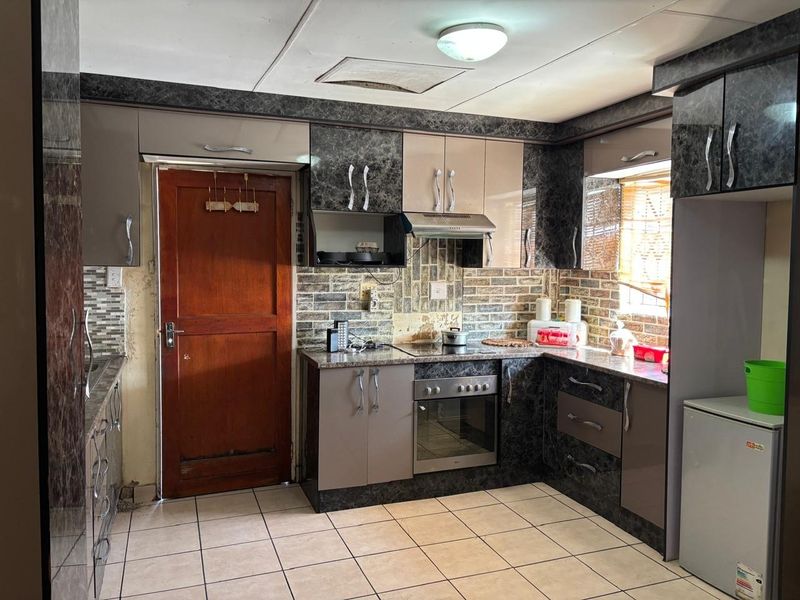 A functional kitchen featuring built-in cabinetry, tiled backsplash, and integrated cooking appliances, offering a practical layout with direct exterior access.
