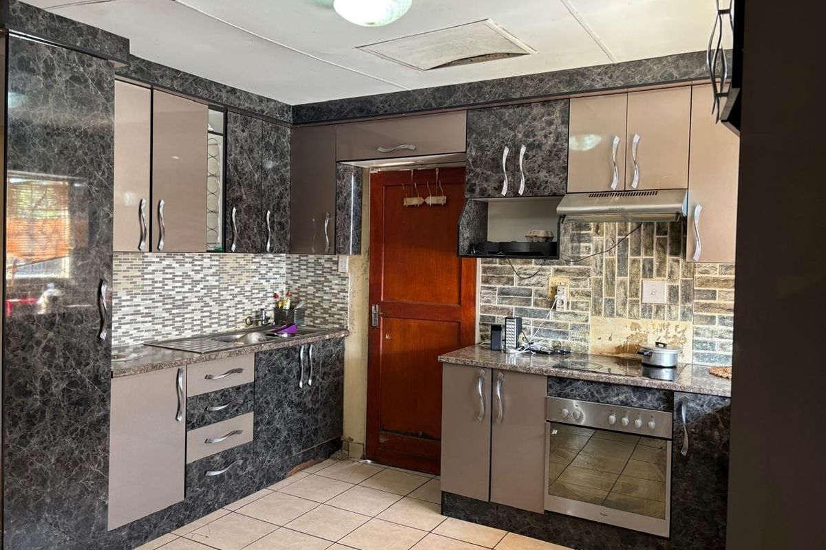 A functional kitchen featuring dark marble-effect cabinetry, built-in oven and hob, tiled backsplash, and tiled flooring, requiring some cosmetic updates to finishes.