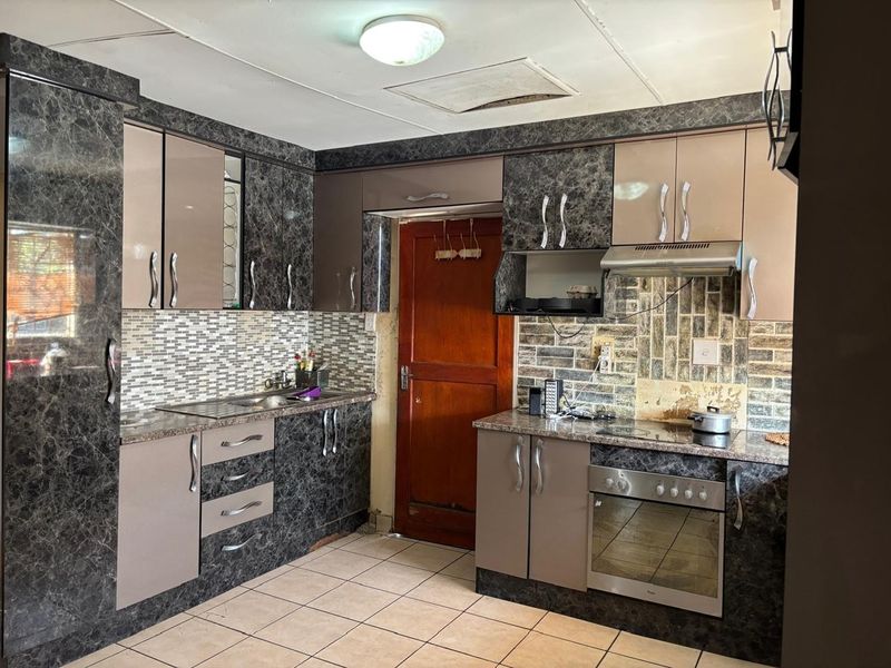 A functional kitchen featuring dark marble-effect cabinetry, built-in oven and hob, tiled backsplash, and tiled flooring, requiring some cosmetic updates to finishes.