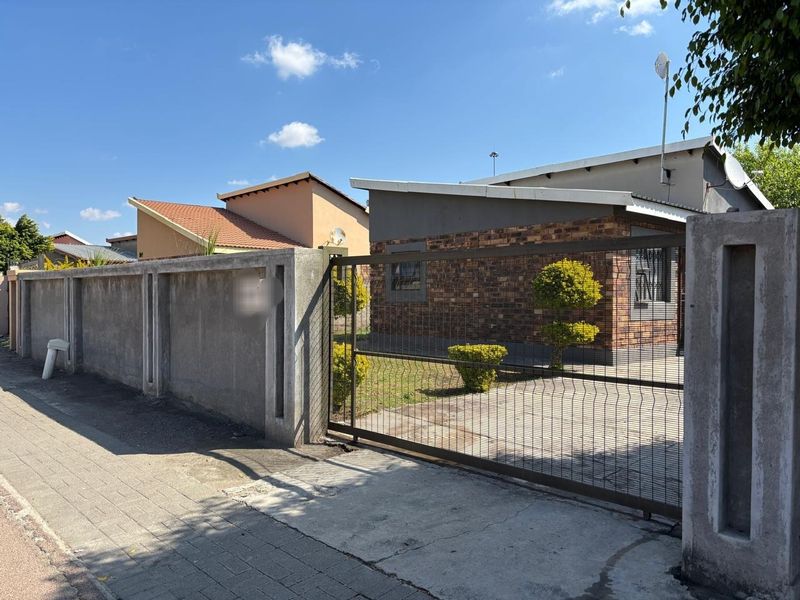 Front view of a face brick house featuring a secure metal sliding gate, paved driveway, and concrete boundary wall.