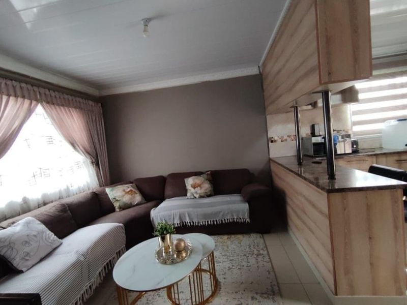Open plan living area featuring a kitchen with breakfast bar, granite countertops, and tiled flooring, seamlessly connected to the lounge space.