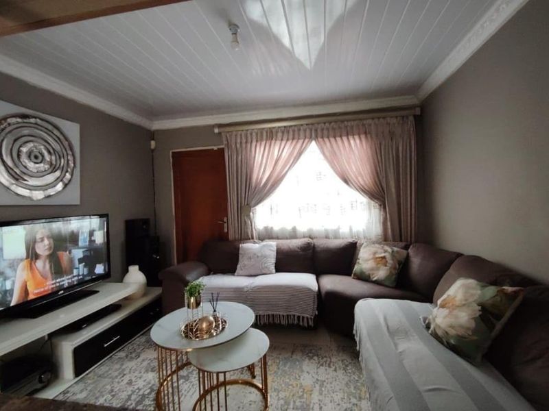 A cozy living room featuring a tongue and groove ceiling with decorative cornice and window curtain rails.
