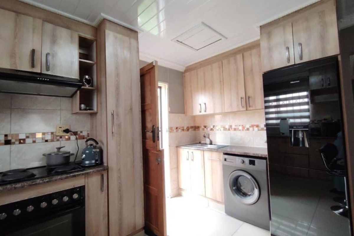 A functional kitchen featuring light wood-finish cabinetry, tiled backsplash, integrated oven and hob, and space for laundry appliances.