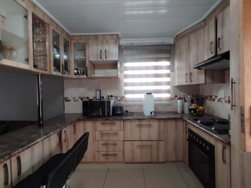 A functional kitchen featuring wood-look laminate cabinetry, stone-effect countertops, built-in oven, electric hob, and tiled flooring with a window providing natural light.