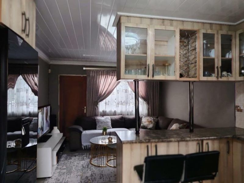 Open-plan living area featuring a kitchen with breakfast bar, glass-fronted cabinetry, and a connected lounge space with neutral finishes.