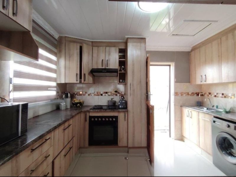 A functional kitchen featuring light wood-finish cabinetry, dark laminate countertops, built-in oven and hob, tiled backsplash, and direct access to the exterior.