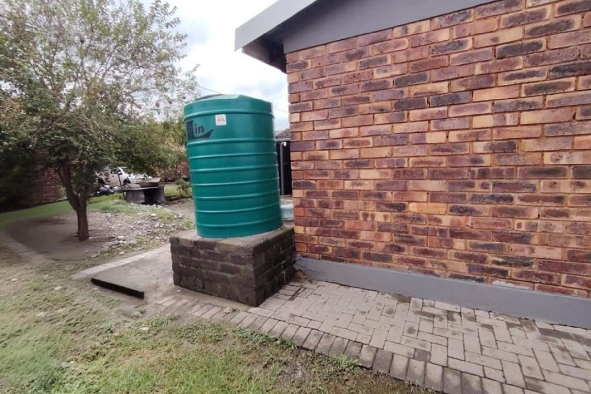 Rear exterior view featuring a water tank on a brick plinth, set against a face brick wall with paved ground area.