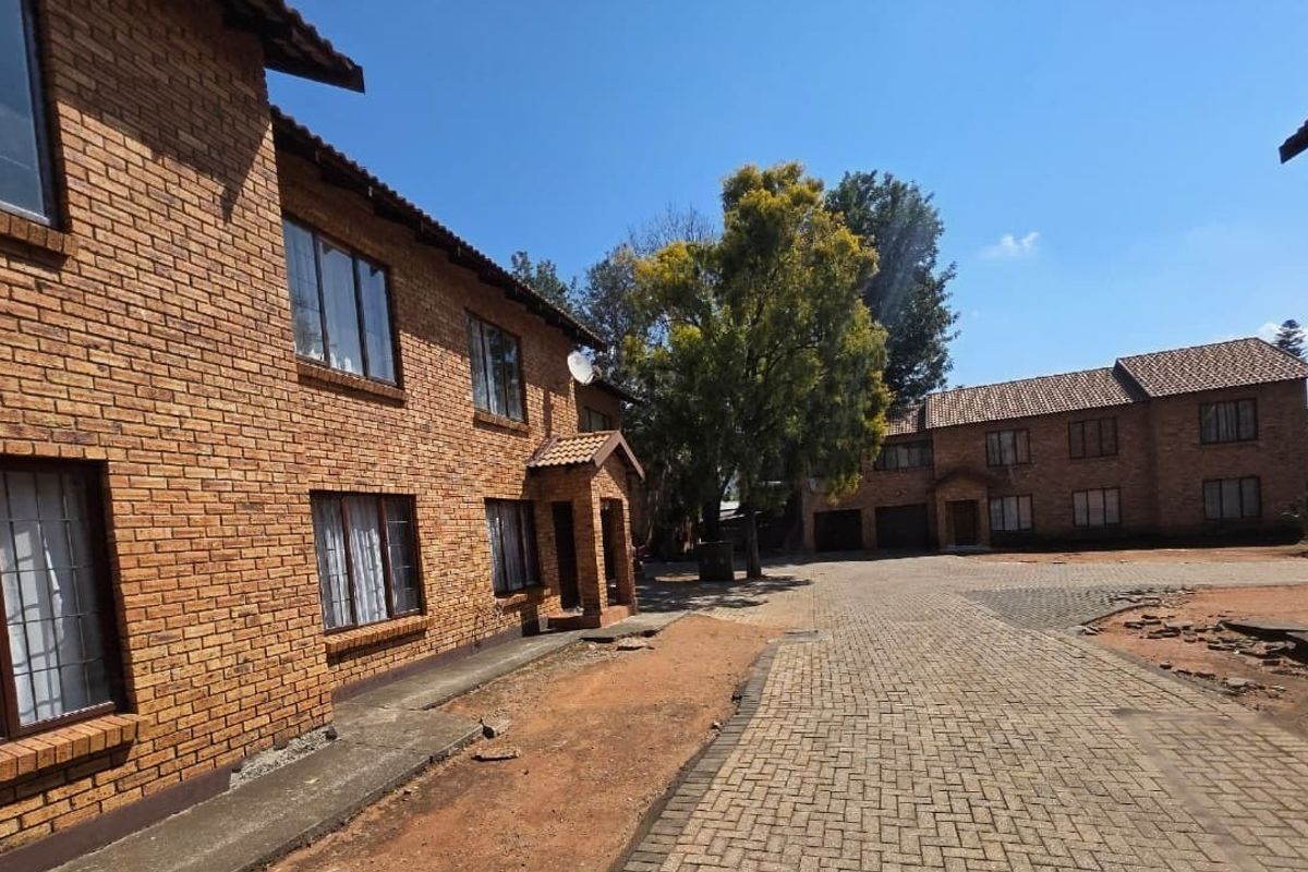 Exterior view of a face brick apartment complex featuring a paved driveway and established trees in the communal courtyard area.