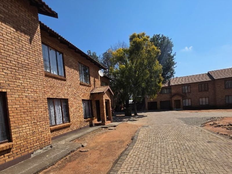 Exterior view of a face brick apartment complex featuring a paved driveway and established trees in the communal courtyard area.