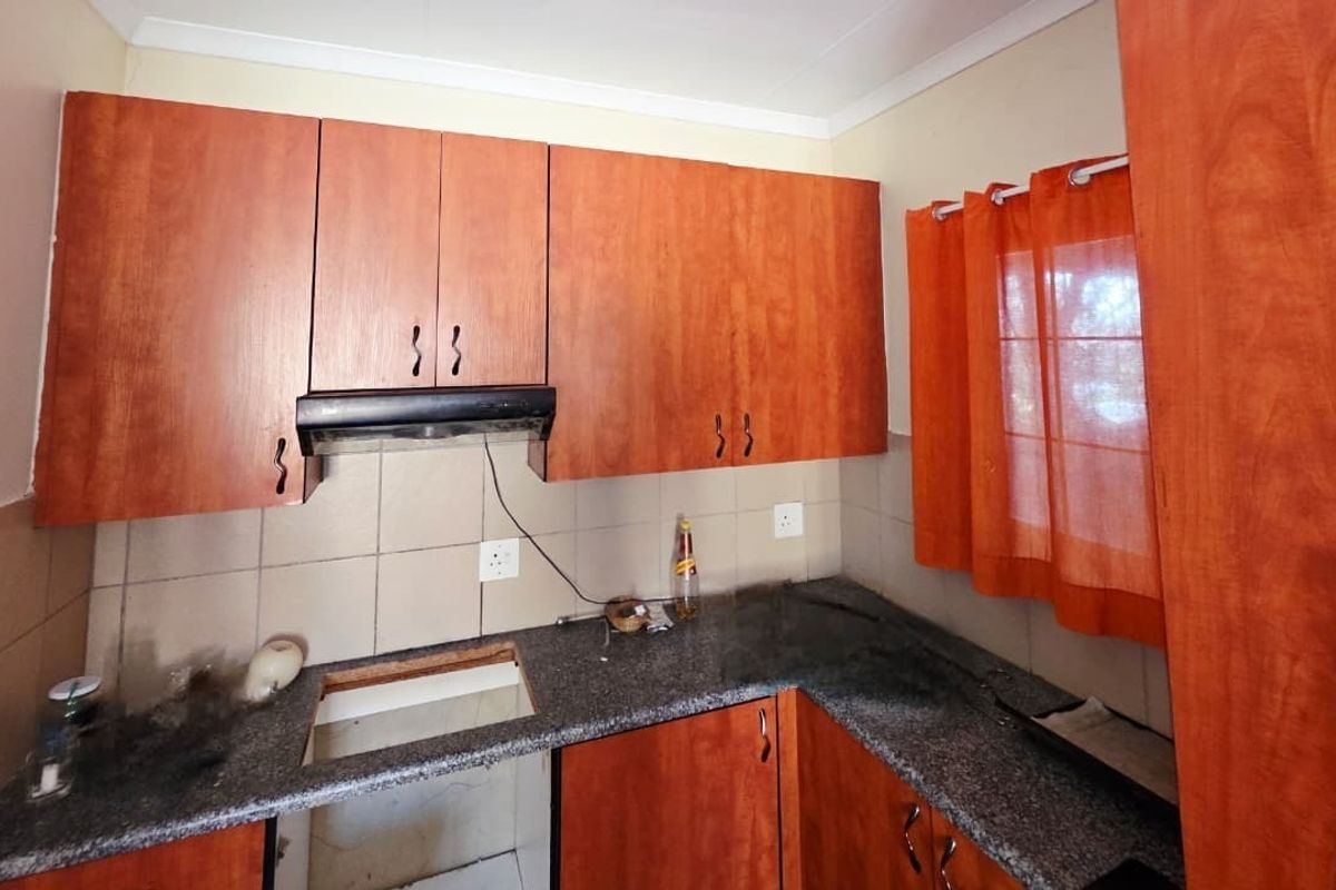 A compact kitchen featuring granite countertops, tiled backsplash, and wooden cabinetry, currently requiring a new cooktop installation.