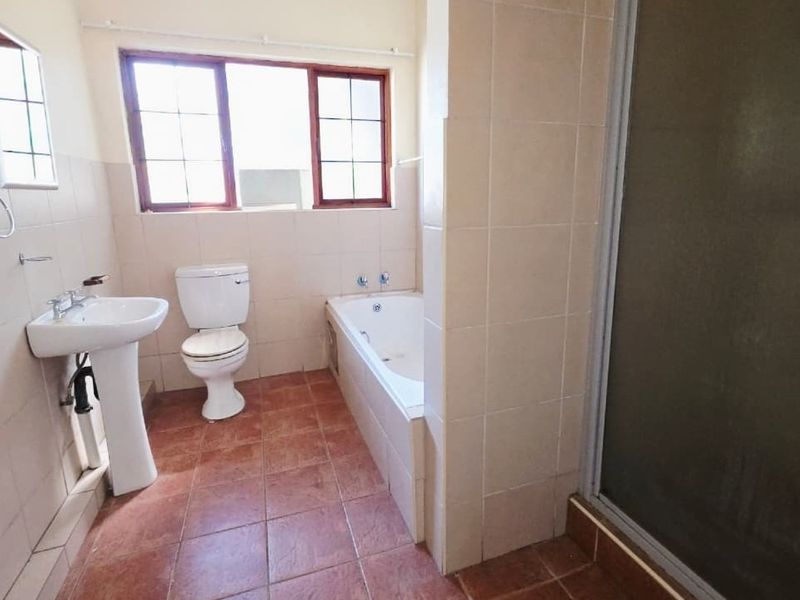 A functional bathroom featuring a pedestal basin, toilet, built-in bathtub, and a separate shower enclosure with tiled finishes throughout.