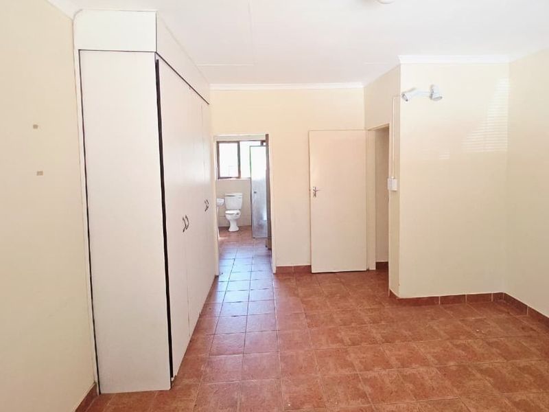 An empty bedroom featuring built-in cupboards, tiled flooring, and direct access to an en-suite bathroom.