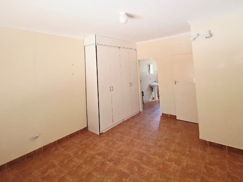 An empty bedroom featuring tiled flooring, built-in cupboards, and access to an adjoining bathroom area.