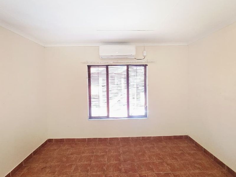 An empty bedroom featuring tiled flooring, a wall-mounted split-system air conditioner, and window blinds.