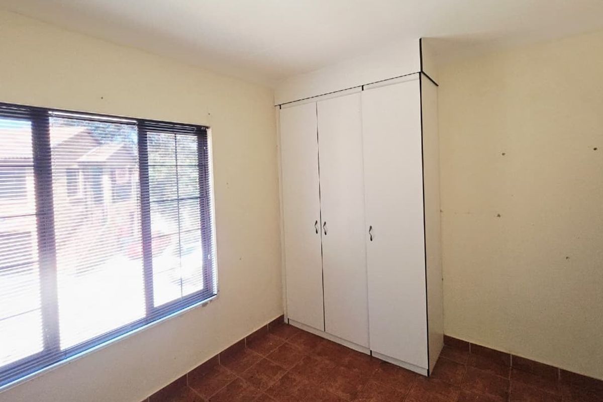 A vacant bedroom featuring tiled flooring, a built-in wardrobe, and a large window with fitted venetian blinds.