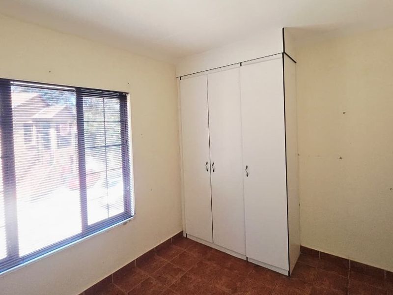 A vacant bedroom featuring tiled flooring, a built-in wardrobe, and a large window with fitted venetian blinds.