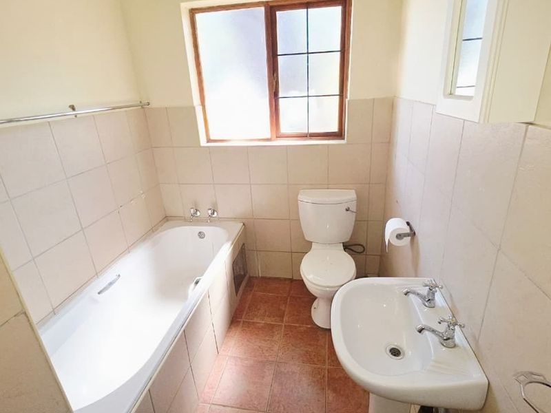 A functional bathroom featuring a bathtub, pedestal basin, and toilet with neutral wall and floor tiling.