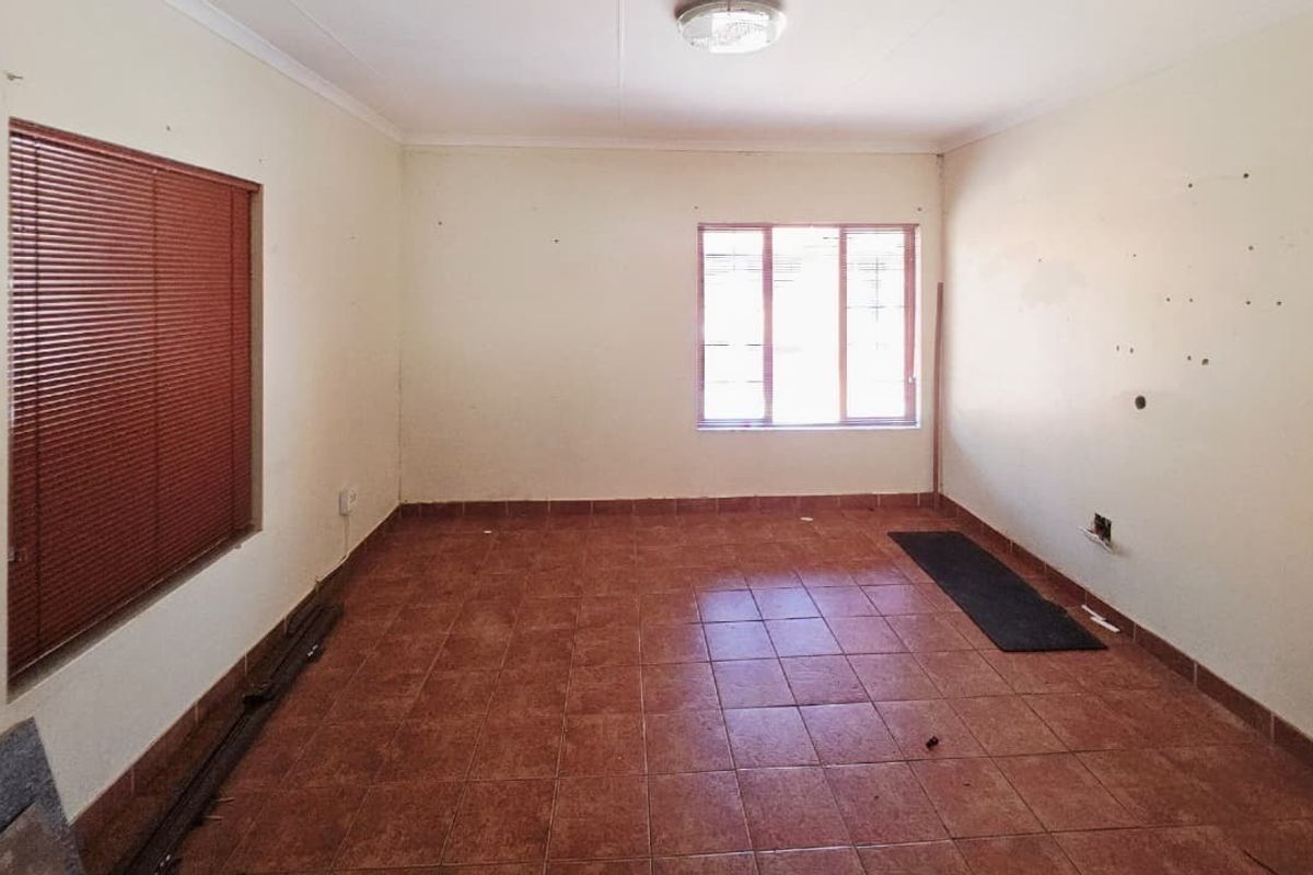 An empty living room featuring ceramic tile flooring, natural light from two windows with venetian blinds, and neutral wall finishes.