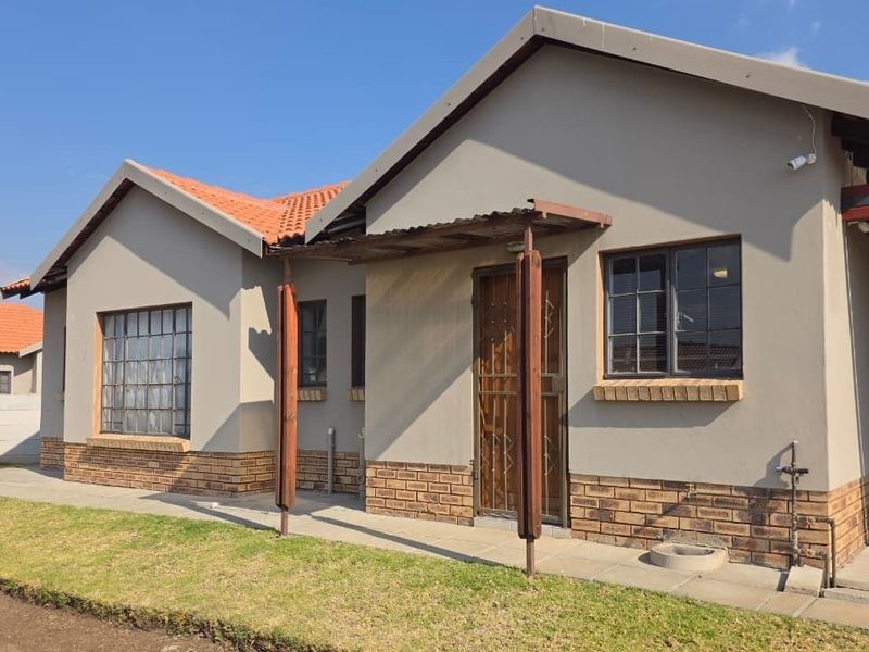 Front elevation of a single-story house featuring a terracotta tiled roof, brick base detailing, and a covered entrance area with security gate.