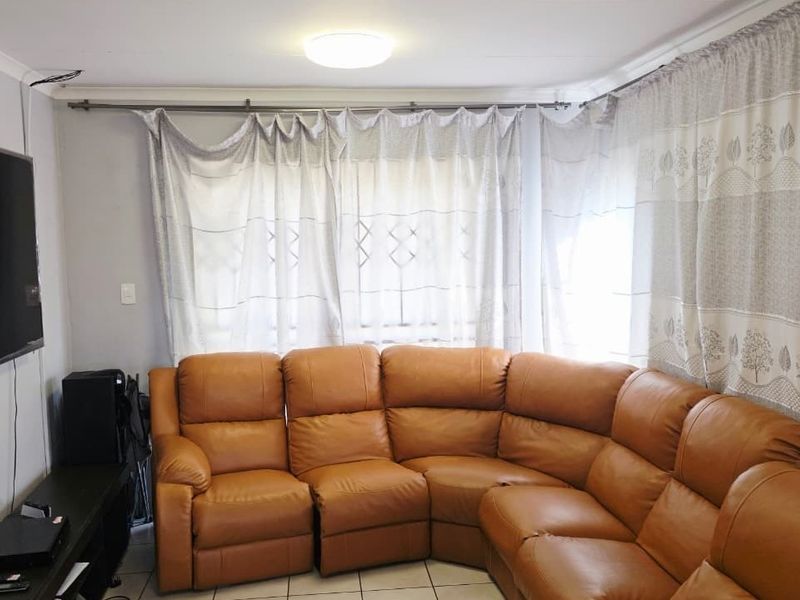 A living room featuring tiled flooring and natural light filtered through curtains, providing a functional and comfortable space.