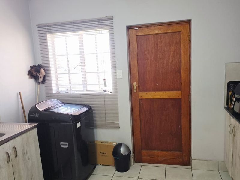 Functional laundry area featuring built-in cabinetry, a stainless steel sink, tiled flooring, and direct access to the exterior via a timber door.