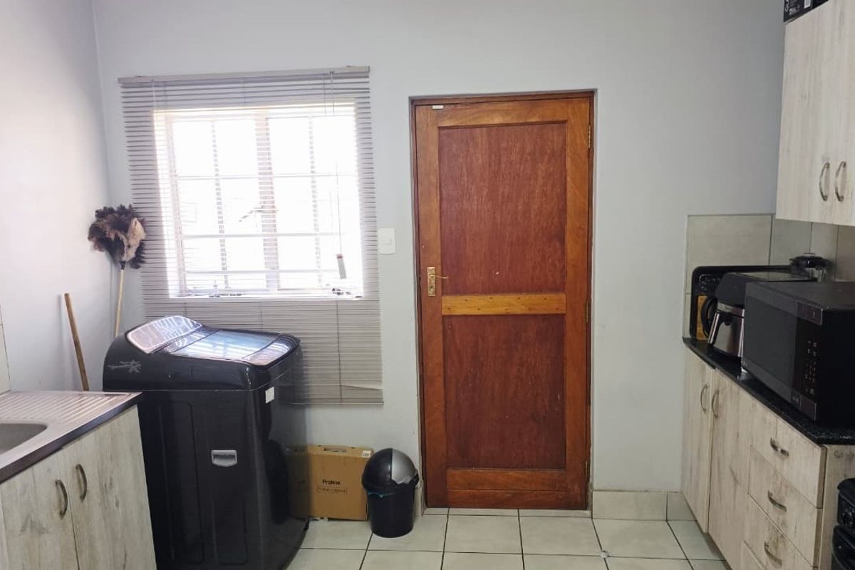 A functional kitchen area featuring built-in cabinetry, tiled flooring, and a window with venetian blinds, providing a practical workspace.