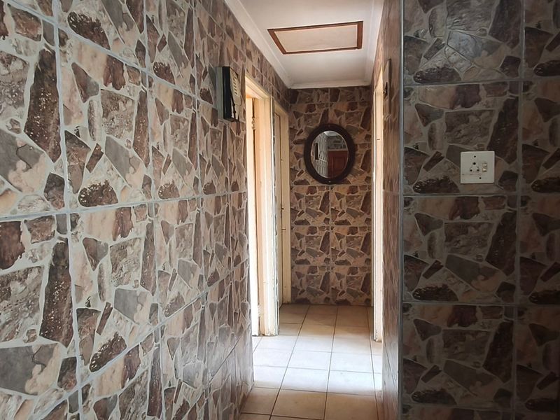 A narrow hallway featuring dated stone-effect wall tiles and neutral floor tiles, providing access to multiple rooms within the home.