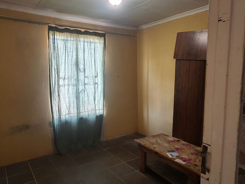 A simple bedroom featuring tiled flooring and yellow painted walls, requiring cosmetic updates to improve its overall condition and appeal.