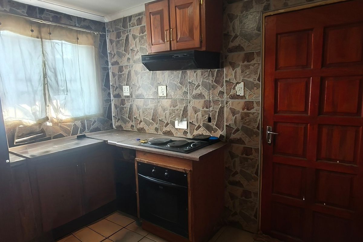A compact kitchen featuring built-in wooden cabinetry, an integrated oven and hob, and distinctive stone-look wall tiling.