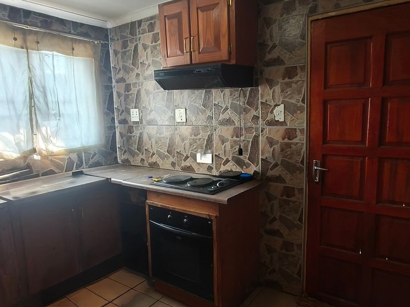 A compact kitchen featuring built-in wooden cabinetry, an integrated oven and hob, and distinctive stone-look wall tiling.