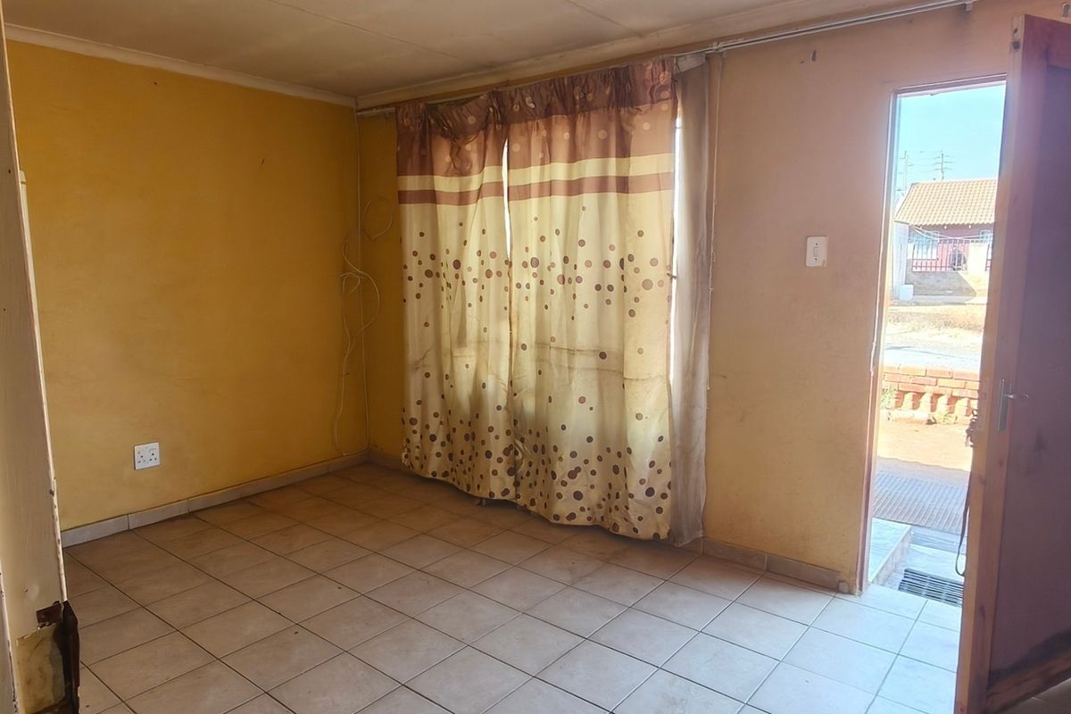 An empty living room featuring tiled flooring, yellow walls, and direct access to the exterior through a wooden door.