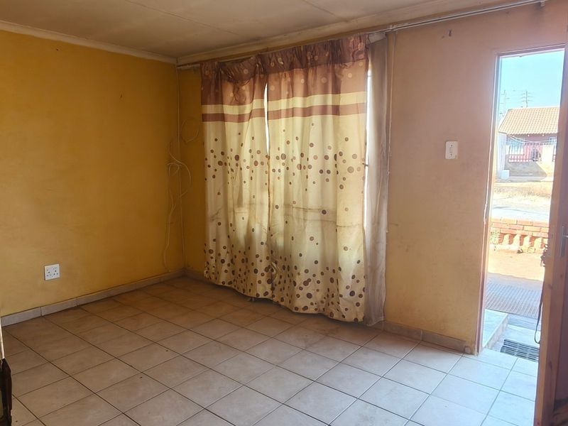An empty living room featuring tiled flooring, yellow walls, and direct access to the exterior through a wooden door.