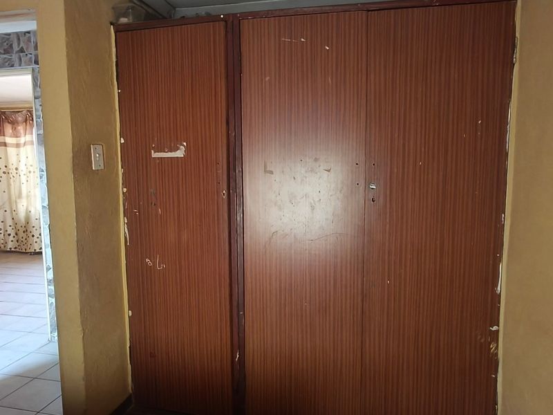 A bedroom interior featuring built-in wooden cupboards, showing signs of wear and tear on the cabinetry and surrounding wall surfaces.