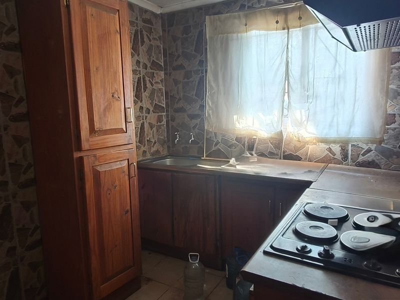 A dated kitchen featuring wooden cabinetry, an electric hob with extractor fan, and stone-effect wall tiling.