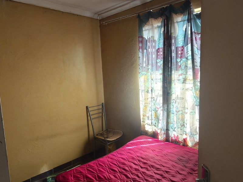 A compact bedroom featuring a built-in cupboard and yellow painted walls, requiring cosmetic updates to improve the overall aesthetic and condition.