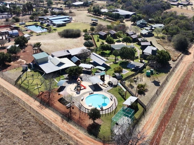 Aerial view of a small holding property featuring multiple outbuildings, a swimming pool, playground area, and extensive grounds with perimeter fencing.