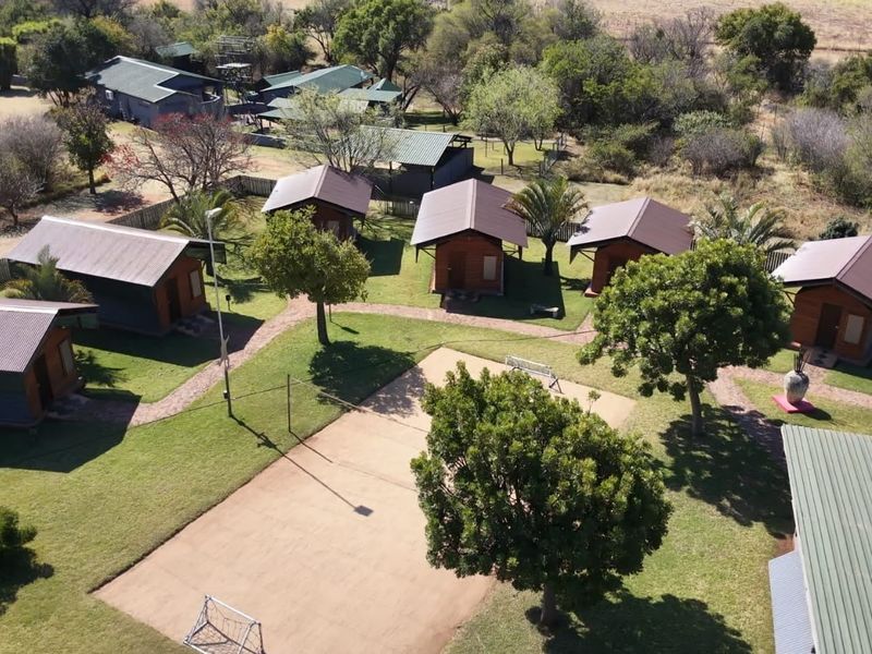 Aerial view of a small holding featuring multiple detached cabin units, a sports court, and well-maintained garden grounds with paved pathways.