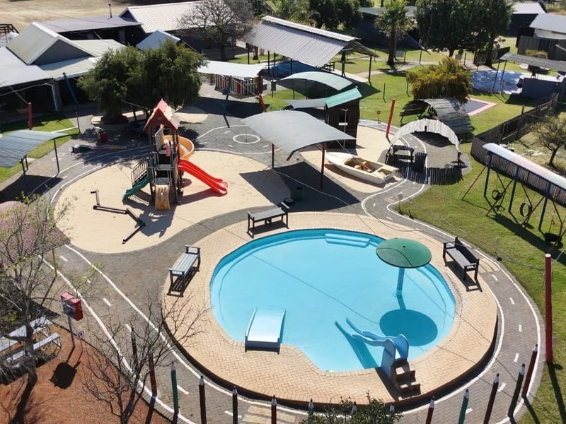 Aerial view of a small holding property featuring a swimming pool, playground area, shade structures, and landscaped grounds.