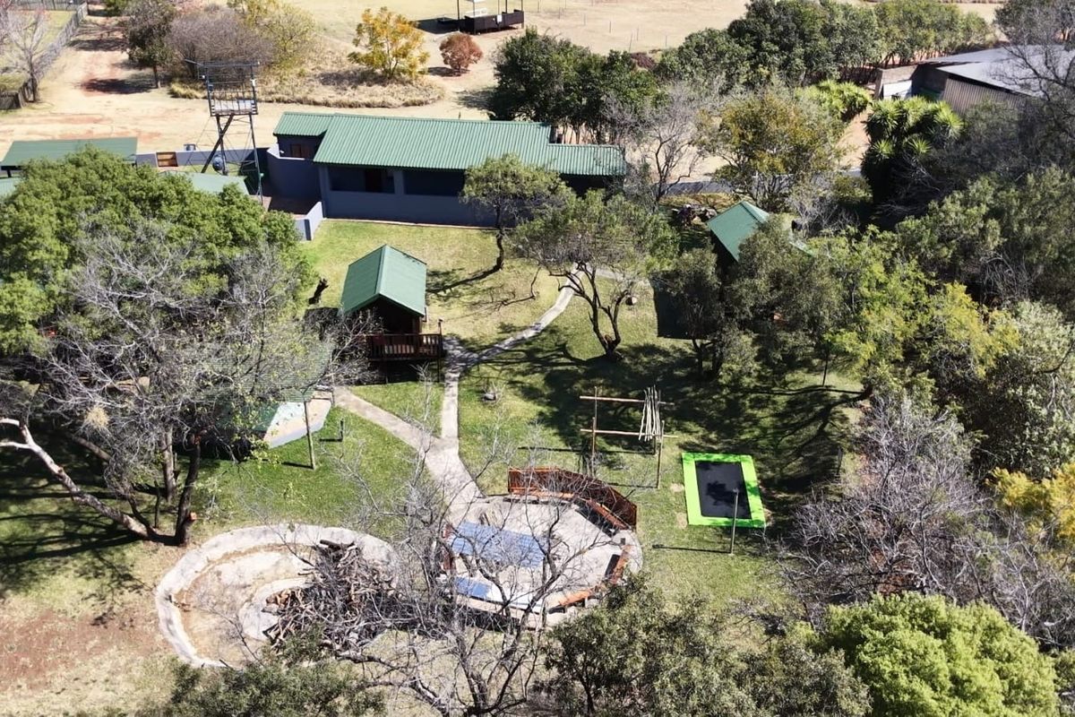 Aerial view of a small holding property featuring multiple outbuildings, landscaped garden areas, paved pathways, and outdoor entertainment spaces including a fire pit.