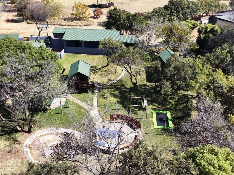 Aerial view of a small holding property featuring multiple outbuildings, landscaped garden areas, paved pathways, and outdoor entertainment spaces including a fire pit.