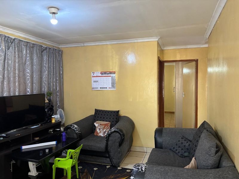 A living room featuring tiled flooring and coved ceilings, requiring cosmetic updates to the wall finishes and ceiling to improve the overall aesthetic.