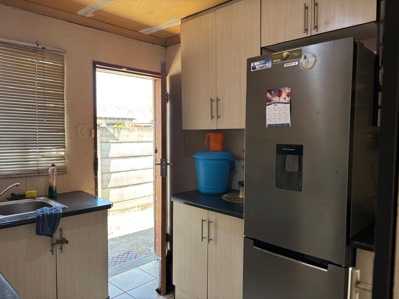 A compact kitchen featuring light wood-finish cabinetry, dark countertops, and direct access to the exterior, requiring some ceiling repairs.