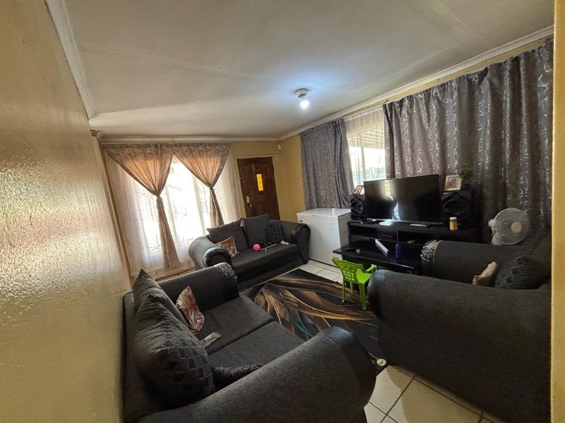 A living room featuring tiled flooring, a timber entrance door, and coved ceilings, requiring cosmetic updates to improve the overall aesthetic.