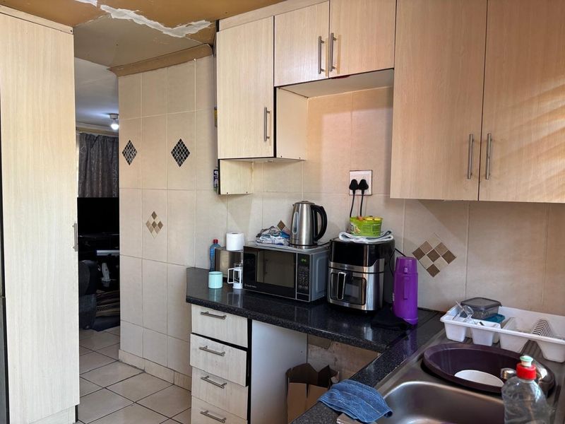 A compact kitchen featuring laminate cabinetry, granite countertops, and tiled finishes, currently showing signs of ceiling damage requiring repair.