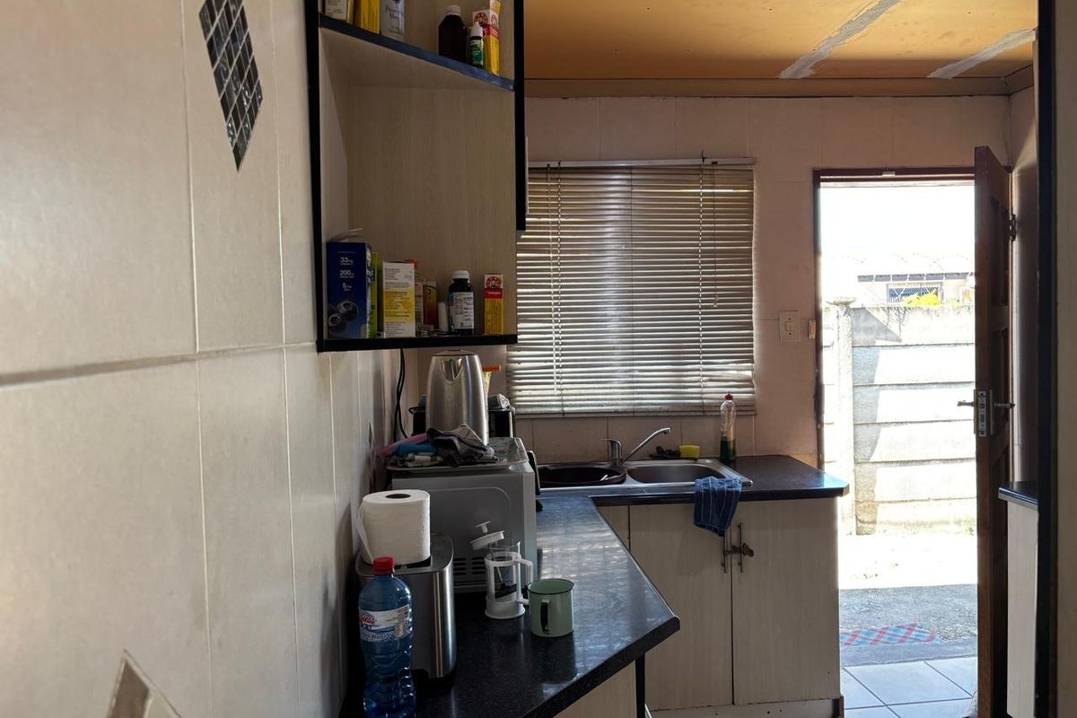 A compact kitchen featuring basic cabinetry, a stainless steel sink, and tiled finishes, with direct access to an outdoor area.