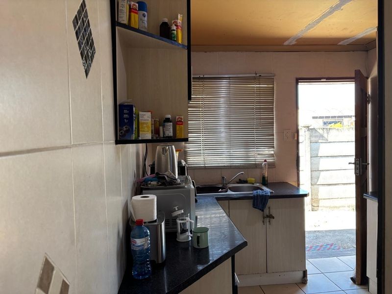 A compact kitchen featuring basic cabinetry, a stainless steel sink, and tiled finishes, with direct access to an outdoor area.