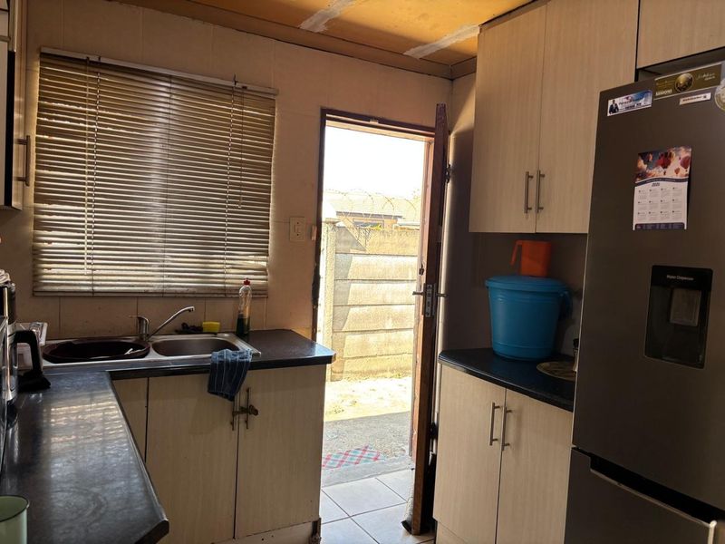 A functional kitchen featuring laminate cabinetry, dark countertops, and a stainless steel sink, with direct access to the rear exterior area.