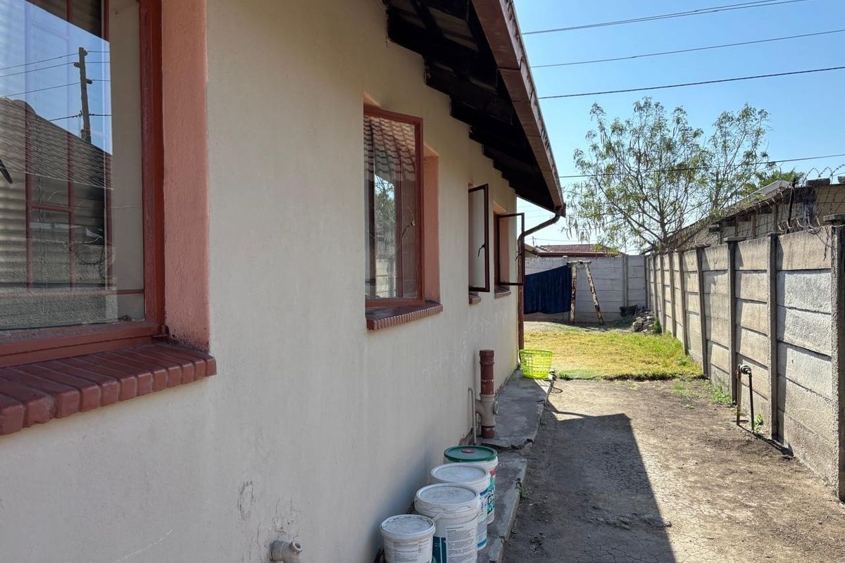 Rear exterior view of the property featuring a concrete boundary wall, steel window frames, and a paved apron along the building side.
