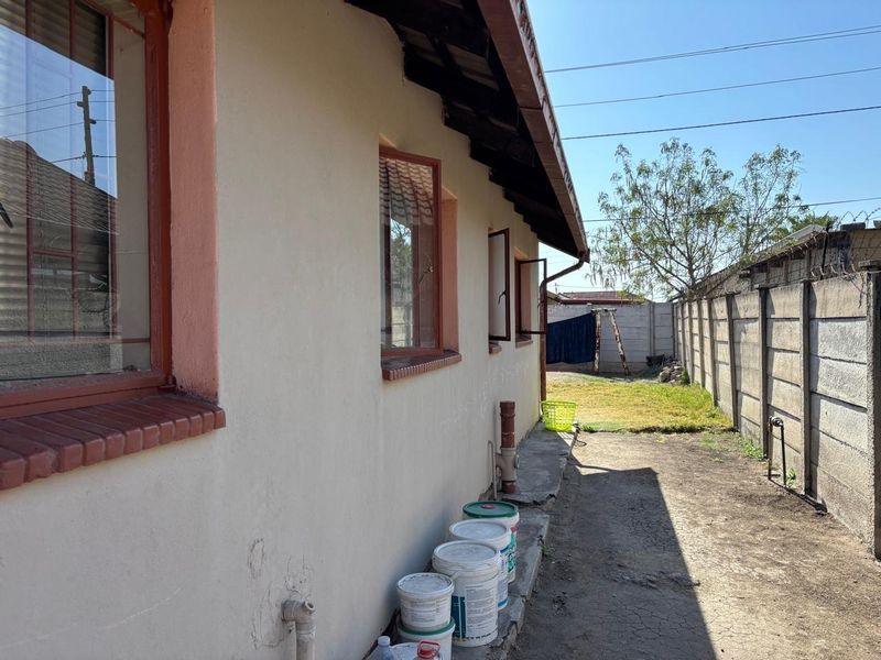 Rear exterior view of the property featuring a concrete boundary wall, steel window frames, and a paved apron along the building side.